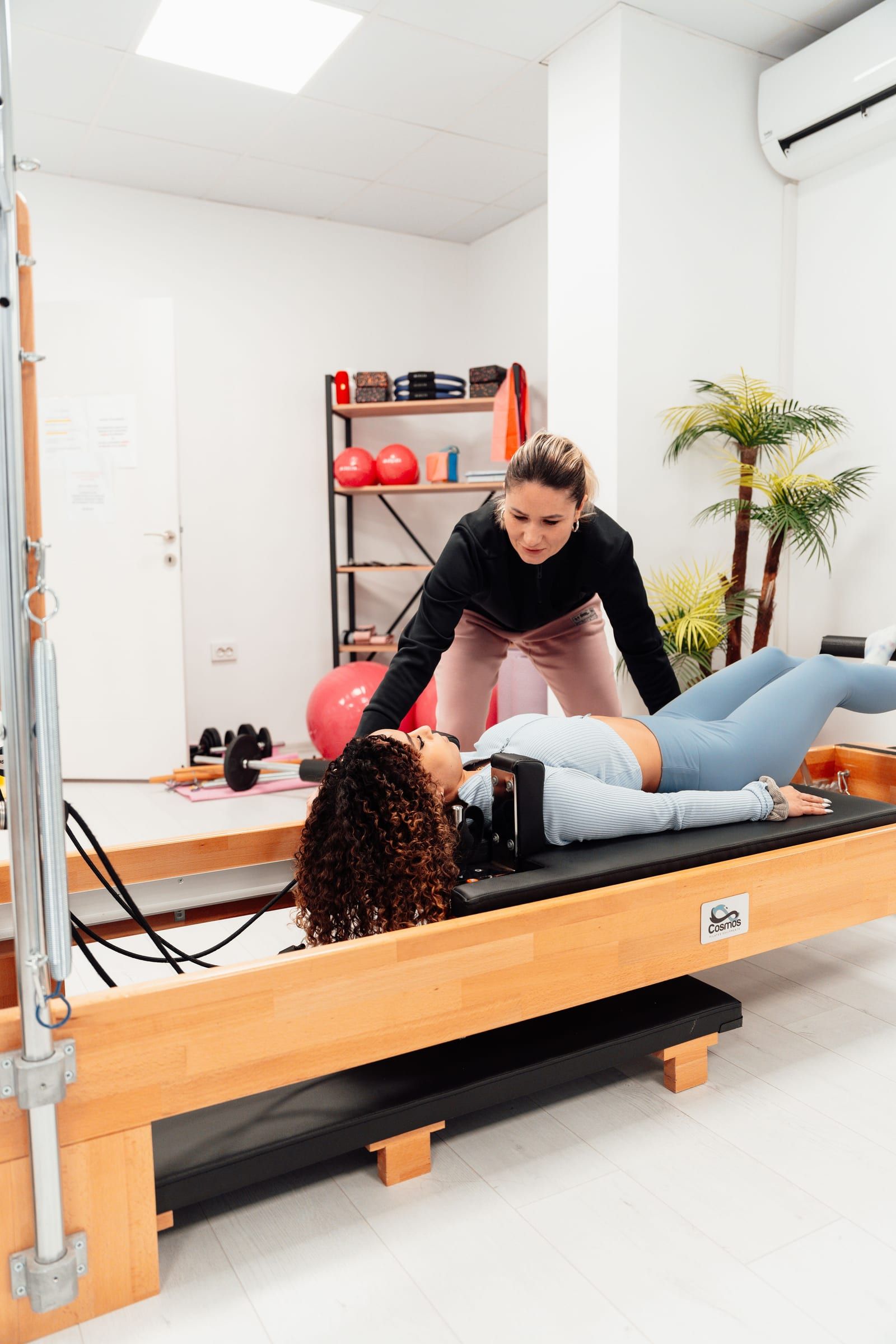 Instructora guiando a una alumna recostada en la máquina Reformer